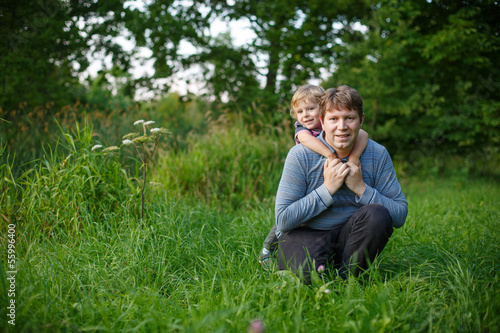 Little boy and his father sitting on grass in summer forest