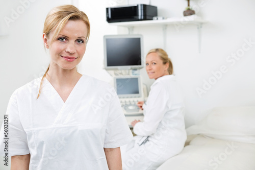 Happy Female Gynecologist With Colleague In Background