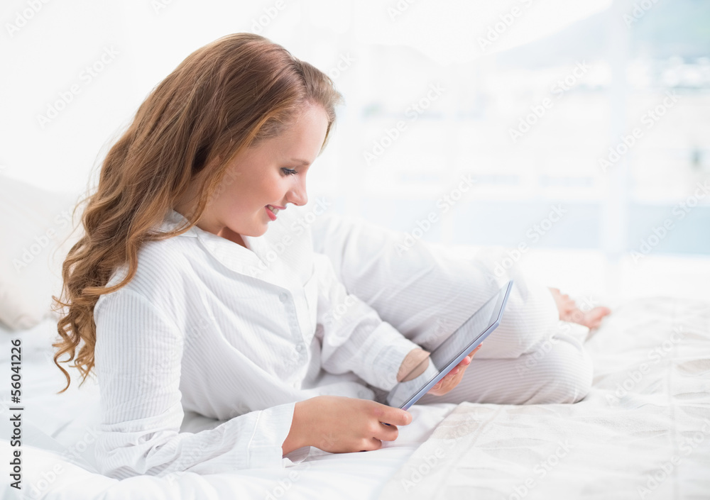 Content pretty woman using a tablet pc lying on her bed Content pretty woman using a tablet pc lying on her bed