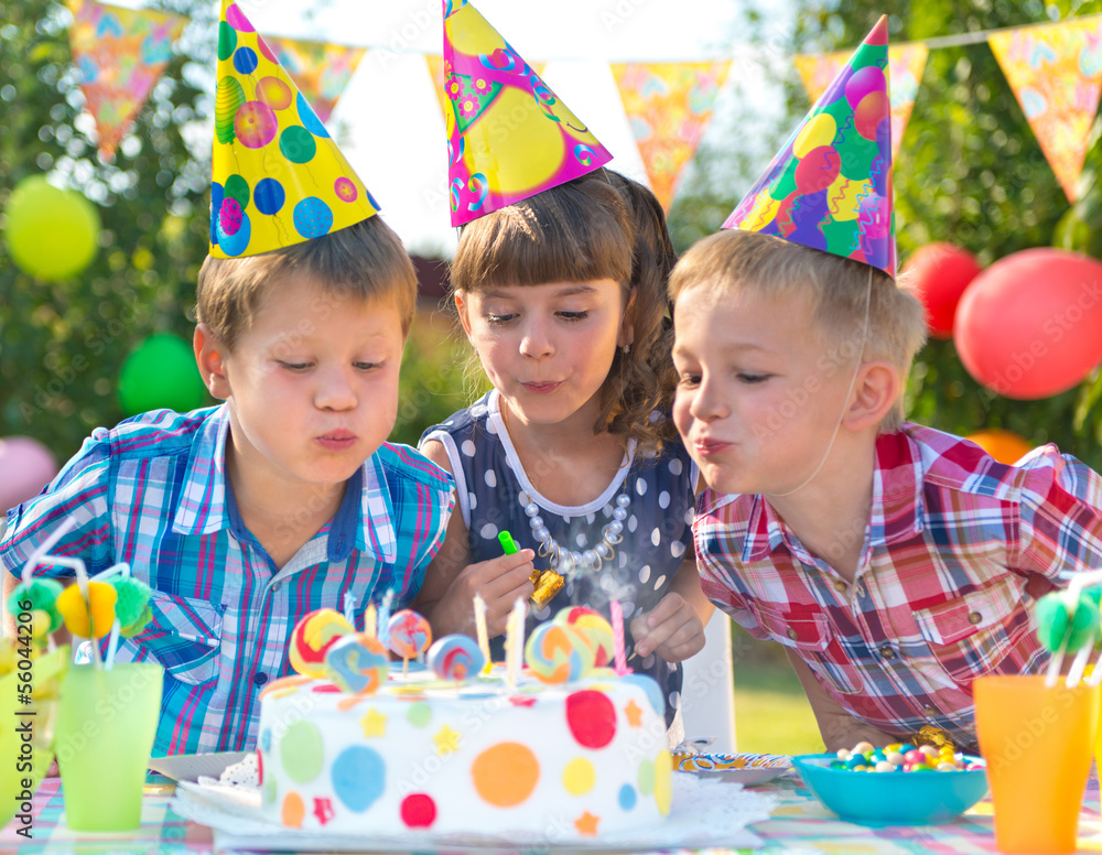 Kids at birthday party blowing candles on cake - obrazy, fototapety, plakaty 