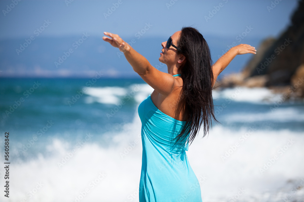 Schlanke Frau steht am Strand und streckt ihre Arme aus