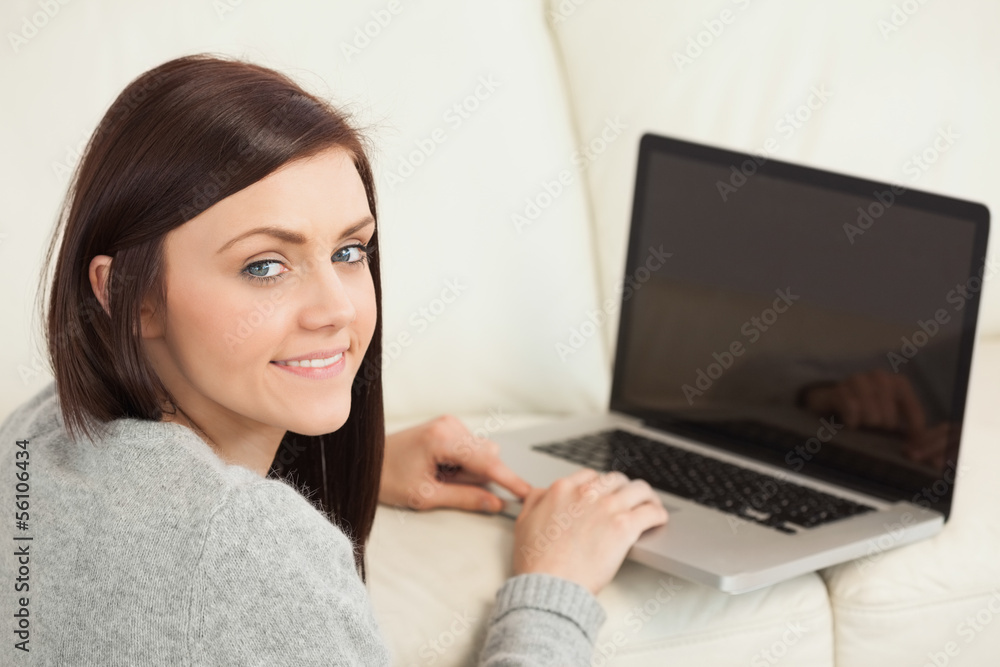 Smiling girl using a laptop on a sofa looking at camera Smiling girl using a laptop on a sofa looking at camera