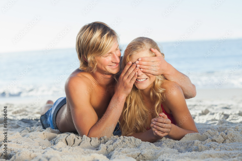 Man covering girlfriends eyes lying on the beach Man covering girlfriends eyes lying on the beach