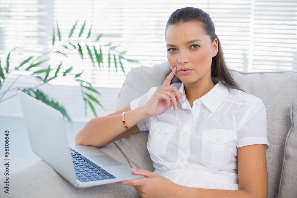 Thoughtful pretty woman using laptop sitting on cosy sofa Thoughtful pretty woman using laptop sitting on cosy sofa