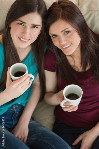 Two smiling friends having coffee and looking at camera on the c