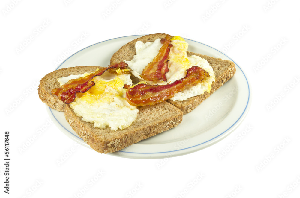 Two slices of brown bread with fried egg and bacon.