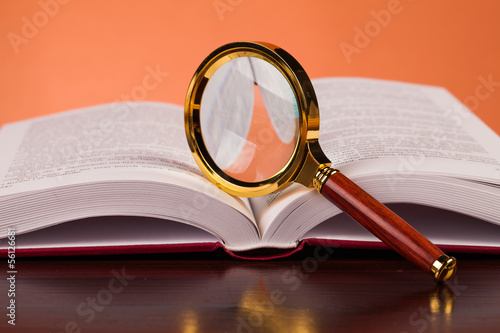 open book on wooden table and magifying glass photo