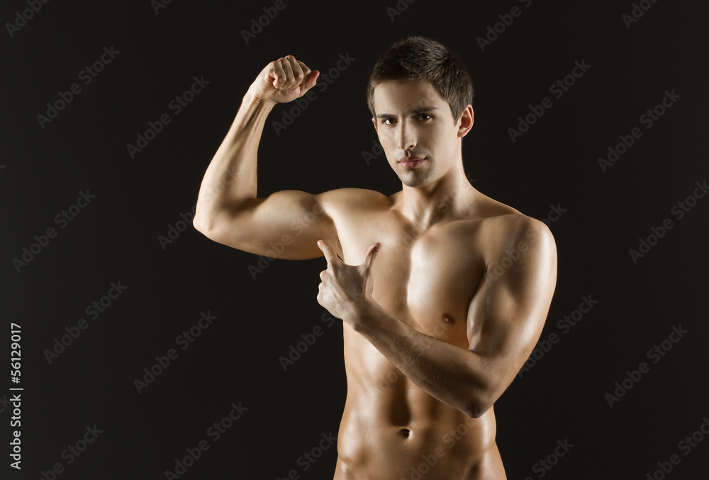 Naked sportsman pointing at his bicep, isolated on black