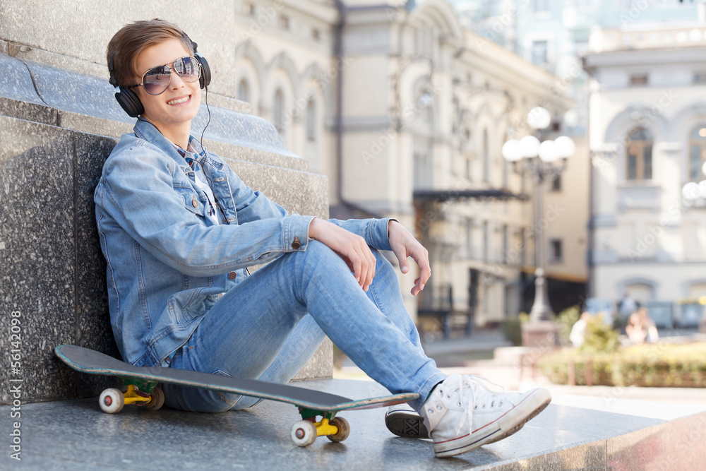 Teenager. Cheerful teenager sitting near his skate and smiling a