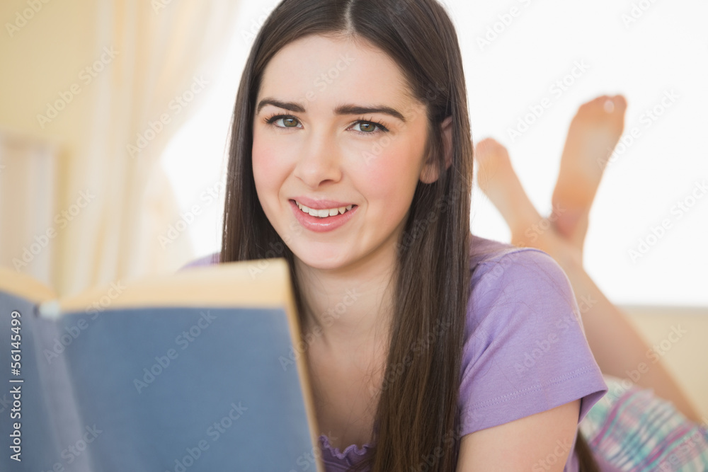 Pretty smiling girl looking at camera and lying on a bed reading Pretty smiling girl looking at camera and lying on a bed reading