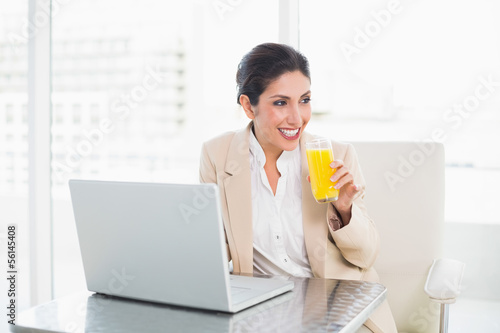 Smiling businesswoman with laptop and glass of orange juice at d