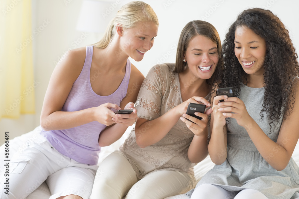 Friends Reading Text Message On Smart Phone In Bedroom Friends Reading Text Message On Smart Phone In Bedroom