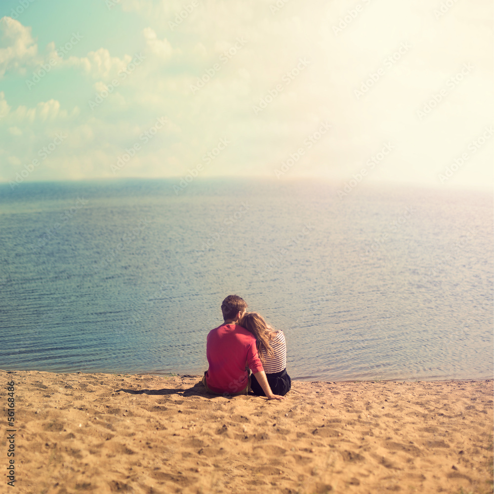 young couple sitting embracing on the sand looking out to sea