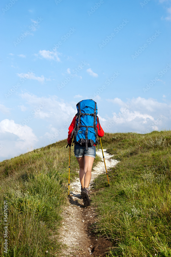 Hiking young woman with backpack and trekking poles