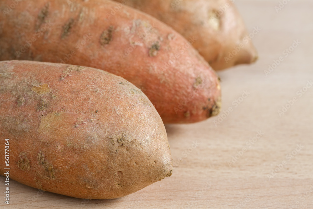Three sweet potatoes on a wooden chopping board Three sweet potatoes on a wooden chopping board