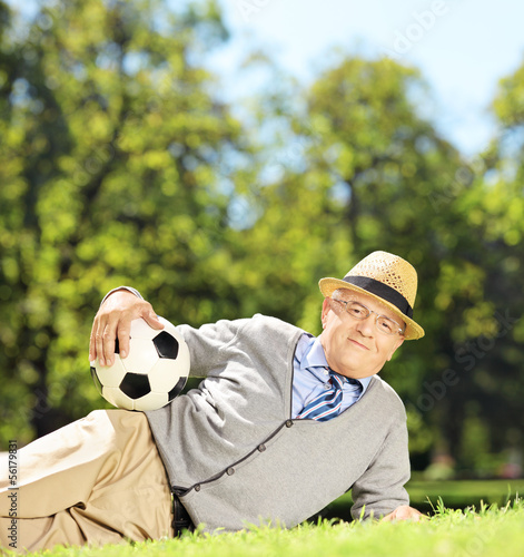 Senior man with hat lying on a grass and holding a soccer ball