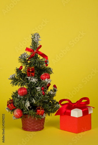Fir-tree in a pot with toys and gifts on a yellow