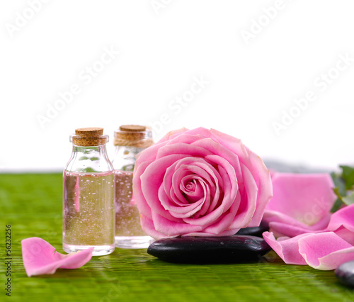 Pink roses with petals and massage oil with stone on green mat photo