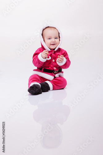 Small boy in Santa suit plays in white studio