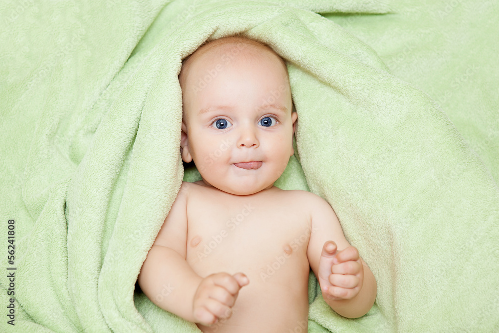 Caucasian baby boy covered with green towel joyfully smiles at c Caucasian baby boy covered with green towel joyfully smiles at c