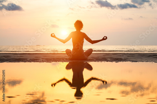 Yoga woman sitting in lotus pose on the beach during sunset.