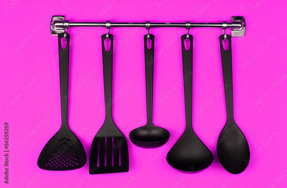 Black kitchen utensils on silver hooks, on pink background Black kitchen utensils on silver hooks, on pink background