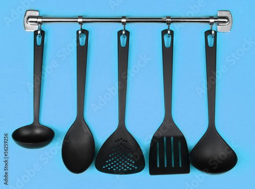 Black kitchen utensils on silver hooks, on blue background