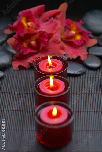 red orchid with row of candle and zen stones on mat