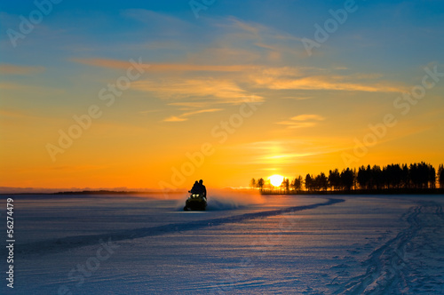 Orange sunset on winter snowy lake and snowmobile with people