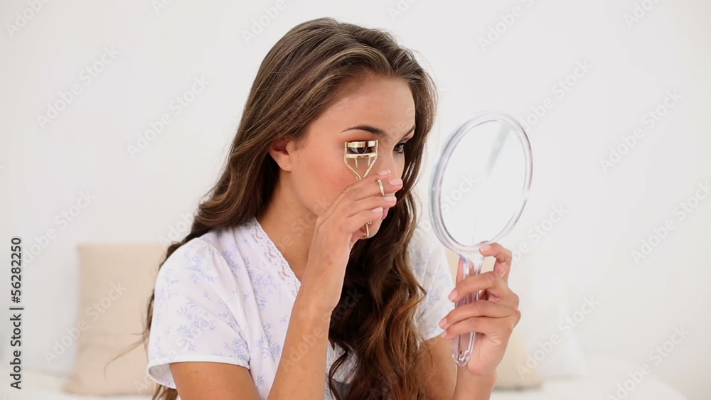Young woman curling her eyelashes and looking in hand mirror Young woman curling her eyelashes and looking in hand mirror