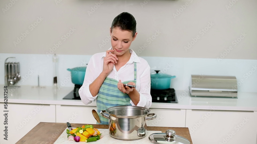 Beautiful brunette sending a text while making dinner Beautiful brunette sending a text while making dinner