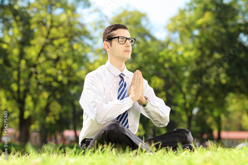 Young businessperson doing yoga exercise seated on a grass