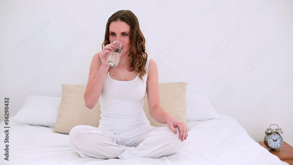 Pretty model sitting on bed drinking glass of water Pretty model sitting on bed drinking glass of water