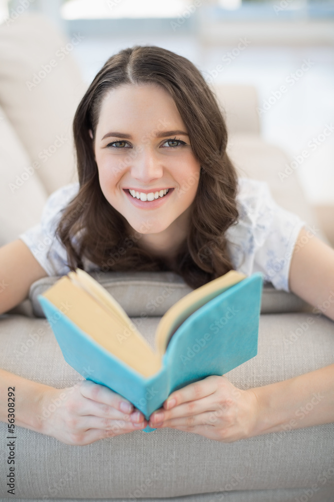 Smiling pretty woman lying on a cosy couch reading book Smiling pretty woman lying on a cosy couch reading book