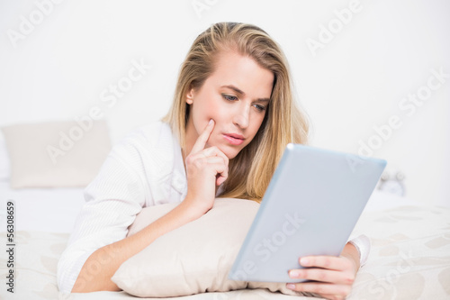 Focused pretty model using her tablet lying on cosy bed