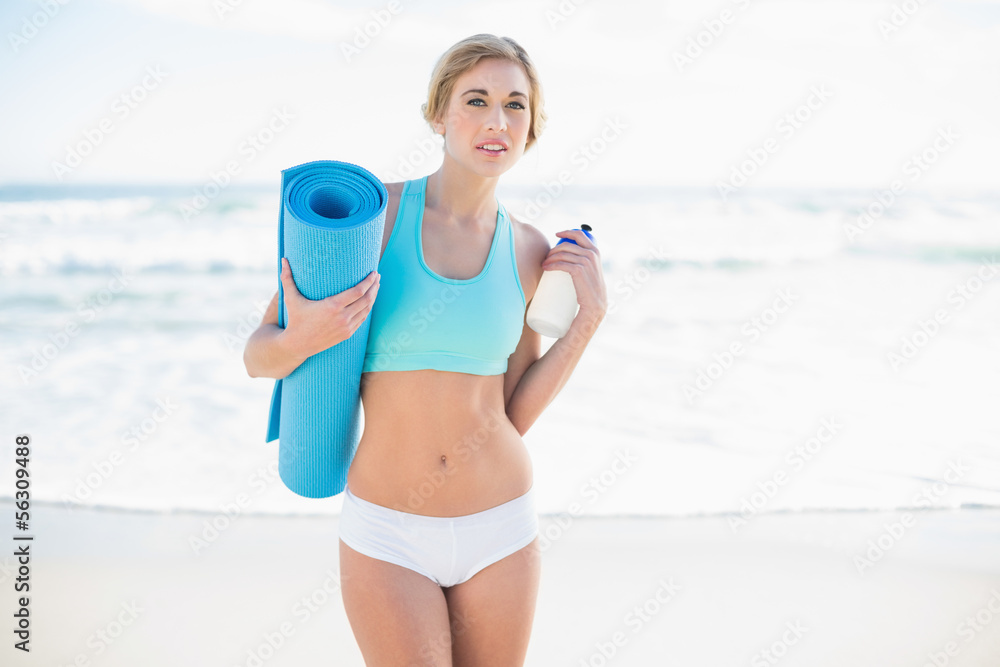 Pensive blonde woman in sportswear holding a bottle and an exerc Pensive blonde woman in sportswear holding a bottle and an exerc