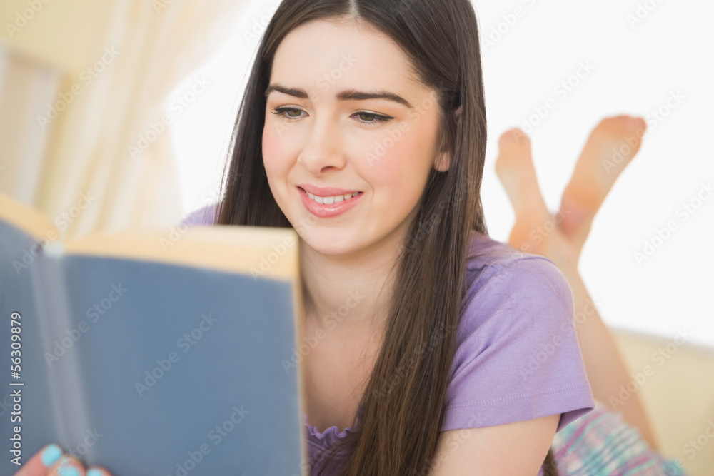 Pretty cheerful girl lying on a bed reading a book Pretty cheerful girl lying on a bed reading a book