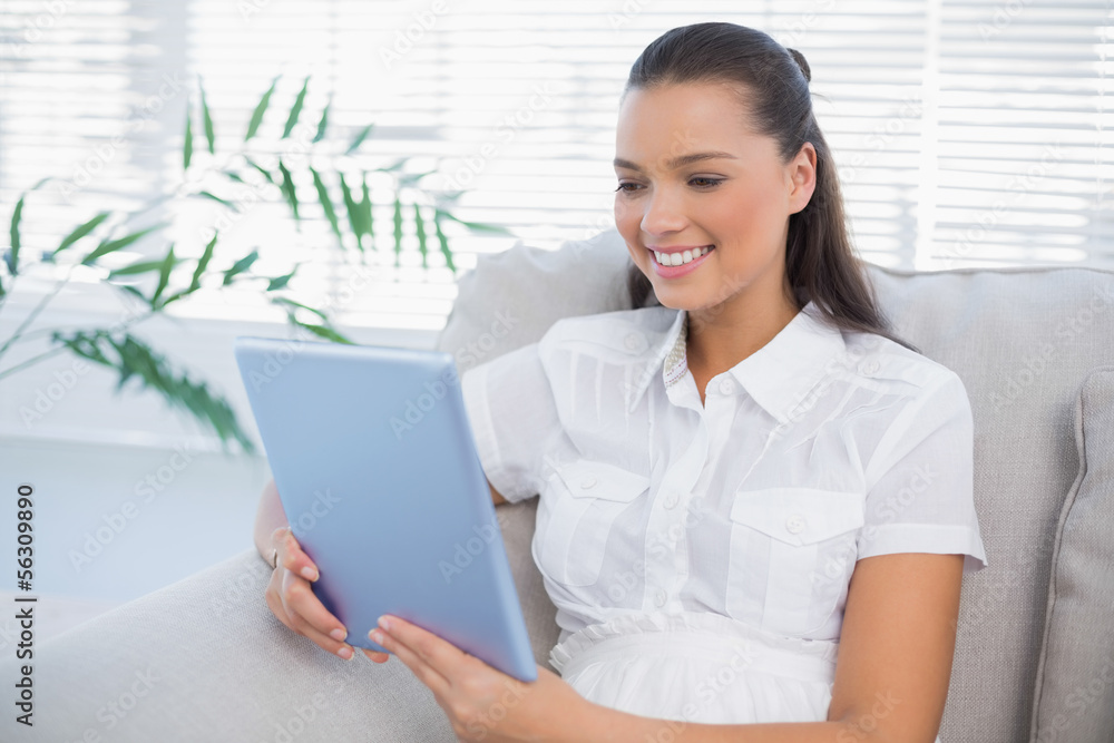 Smiling cute woman using tablet sitting on cosy sofa Smiling cute woman using tablet sitting on cosy sofa