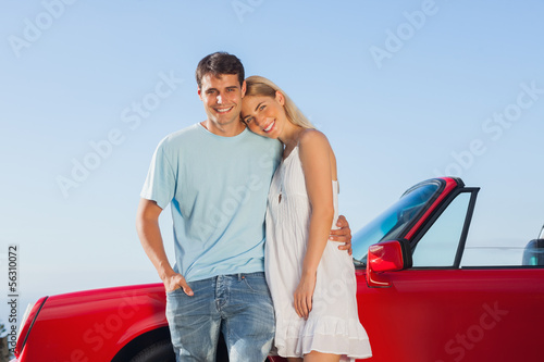 Smiling cute couple posing against their red cabriolet