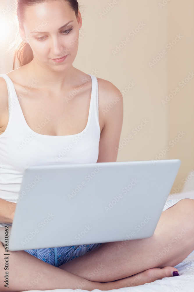 Content brunette sitting on bed using her laptop Content brunette sitting on bed using her laptop