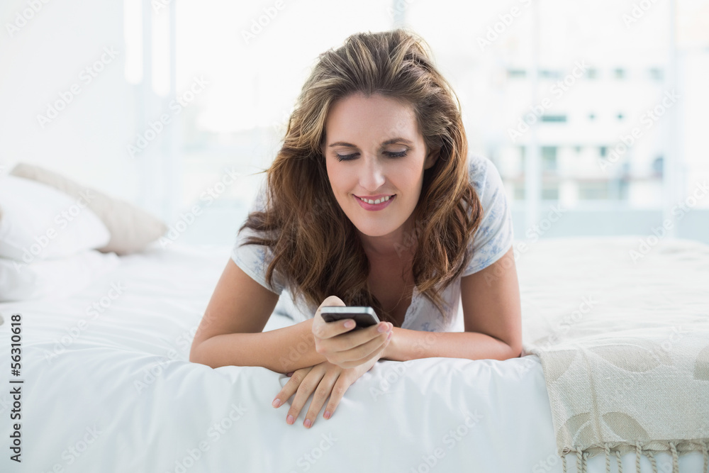 Smiling woman resting in bed text messaging Smiling woman resting in bed text messaging