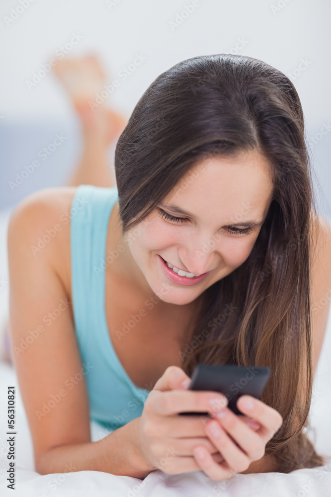Woman using her phone and smiling while on the bed Woman using her phone and smiling while on the bed