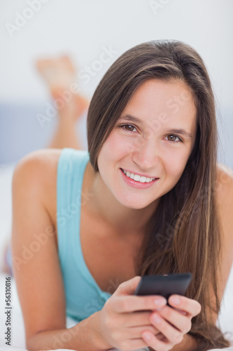 Brunette woman lying in bed with phone