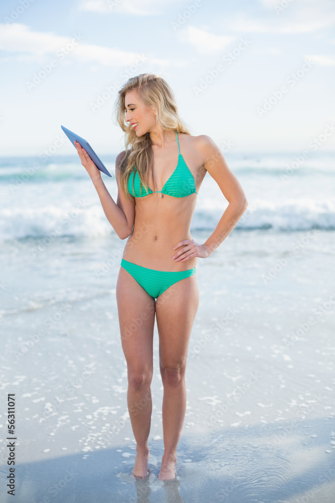 Smiling blonde model in green bikini looking at a tablet pc Smiling blonde model in green bikini looking at a tablet pc