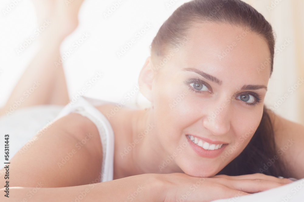 Smiling brunette lying on bed looking at camera