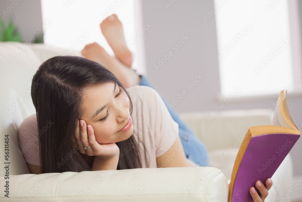 Peaceful asian girl lying on the sofa reading book Peaceful asian girl lying on the sofa reading book