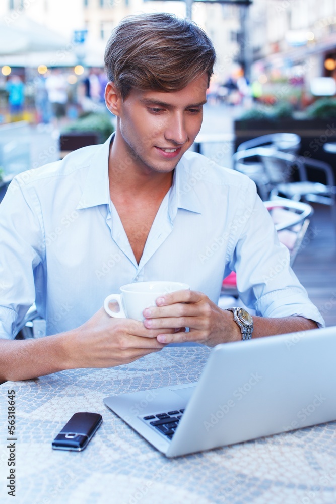 Fototapeta premium Handsome young man with laptop in summer cafe