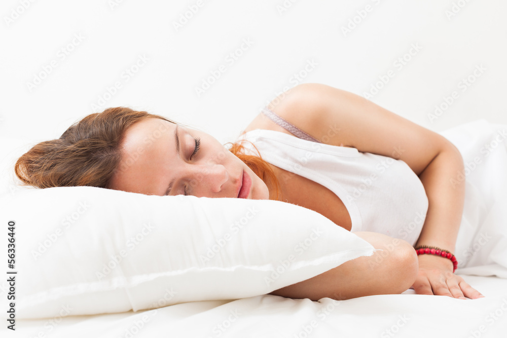 Red-haired woman sleeping on white pillow in bed at home