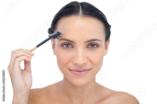 Peaceful young brunette using eyebrow brush