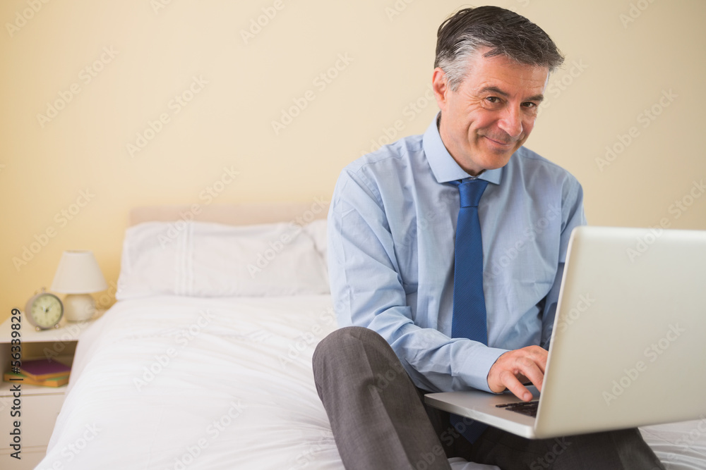Content man using a laptop sitting on a bed Content man using a laptop sitting on a bed